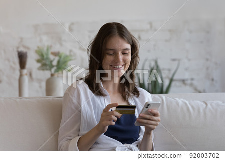 Woman sit on sofa make payment use card and smartphone Woman sit on sofa make payment use card and smartphone 92003702