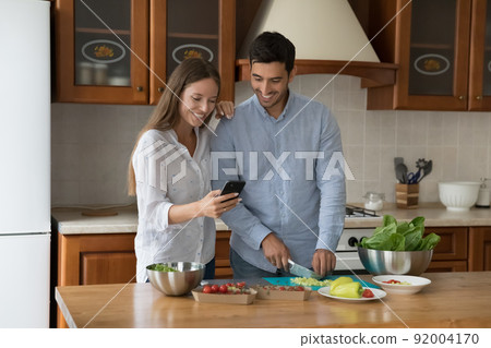 Couple using cellphone making food order while cooking lunch Couple using cellphone making food order while cooking lunch 92004170