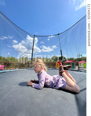 Little girl lying on her stomach on a trampoline 92004172