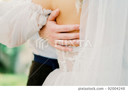 Groom hand on the back of bride in a white lace dress. Close-up 92004248