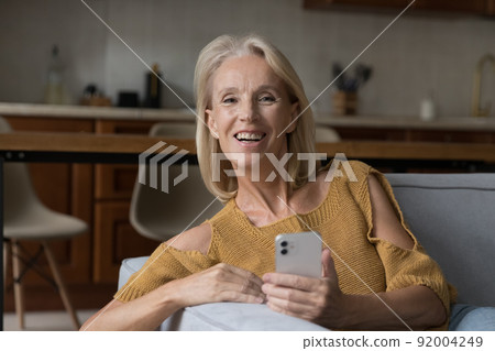 Happy middle-aged woman holds modern smartphone looking at camera 92004249