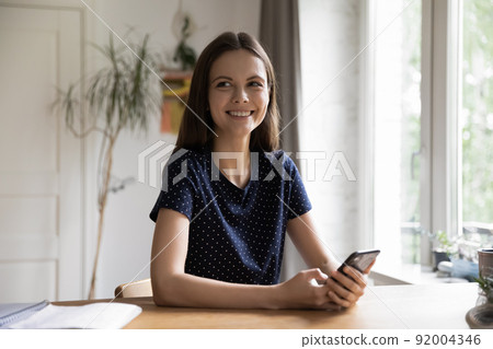 Cheerful millennial young woman using online app on smartphone Cheerful millennial young woman using online app on smartphone 92004346