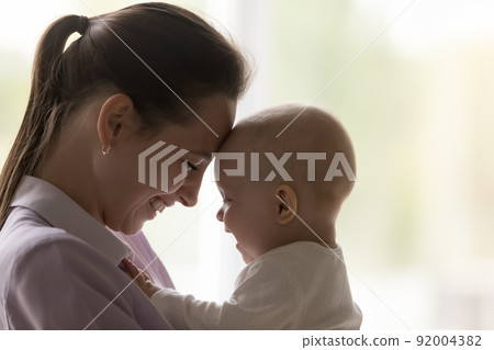 Cute baby and young laughing mother touch foreheads, close up 92004382