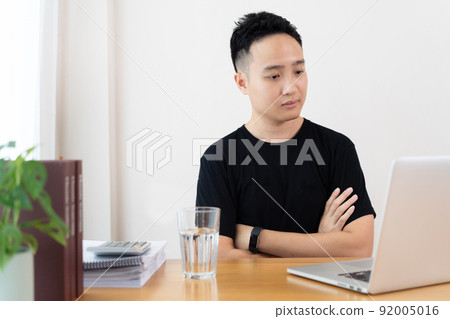 Asian young student using laptop computer for online study at home in the new normal lifestyle. Stressful Asian man making a video conference and meeting while staying at home. Asian young student using laptop computer for online study at home in the new normal lifestyle. Stressful Asian man making a video conference and meeting while staying at home. 92005016
