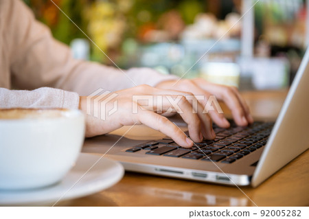 Asian beautiful working woman doing her work and drink in the coffee shop or cafe. Cheerful online blogger writing on her laptop or notebook computer and drinking a coffee close up. Modern lifestyle. Asian beautiful working woman doing her work and drink in the coffee shop or cafe. Cheerful online blogger writing on her laptop or notebook computer and drinking a coffee close up. Modern lifestyle. 92005282