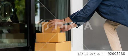 Asian postman with a hygiene protective face mask picking up a parcel package or parcel box from the truck for deliver to customer's door. New Normal concept during covid-19 or coronavirus pandemic Asian postman with a hygiene protective face mask picking up a parcel package or parcel box from the truck for deliver to customer's door. New Normal concept during covid-19 or coronavirus pandemic 92005288
