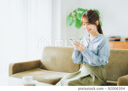 Woman sitting on a sofa and looking at a smartphone Woman sitting on a sofa and looking at a smartphone 92006304
