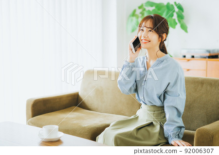 A woman who sits on a sofa and makes a phone call A woman who sits on a sofa and makes a phone call 92006307