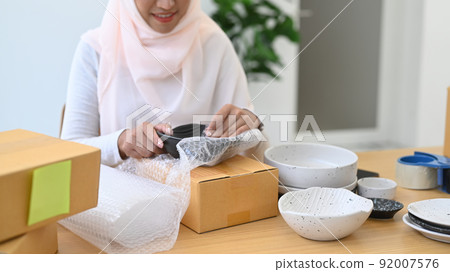 Beautiful young Muslim woman preparing parcel box of product for shipment. Concept of online selling, e-commerce 92007576