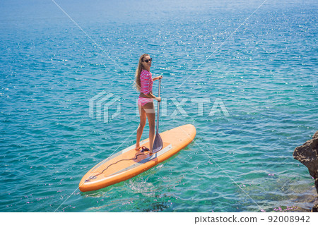 Young women Having Fun Stand Up Paddling in blue water sea in Montenegro. SUP. girl Training on Paddle Board near the rocks 92008942