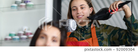Cheerful hairdresser using hairdryer for treatment with clients hairstyle Cheerful hairdresser using hairdryer for treatment with clients hairstyle 92009304