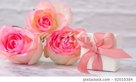 Gift box with tied ribbon bow pink roses on pink background. Greeting card. Present for springtime holidays Copy space for text. Gift box with tied ribbon bow pink roses on pink background. Greeting card. Present for springtime holidays Copy space for text. 92010384