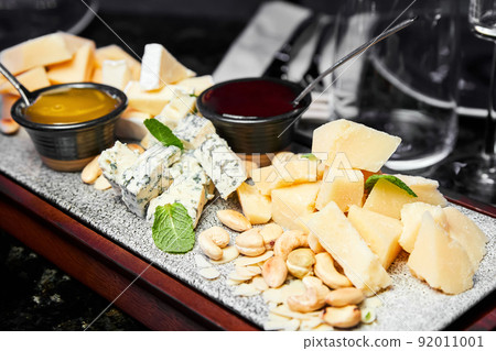 Cheese plate with nuts and honey on a wooden board. Close-up, selective focus 92011001