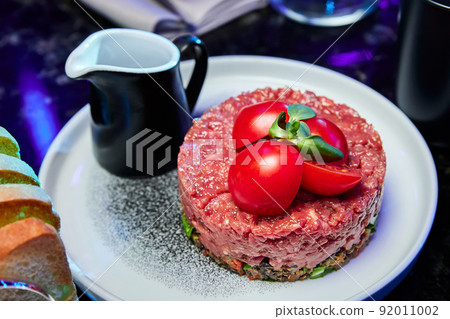 Veal tartare with Tomatoes on a white plate in a restaurant. Close-up, selective focus Veal tartare with Tomatoes on a white plate in a restaurant. Close-up, selective focus 92011002