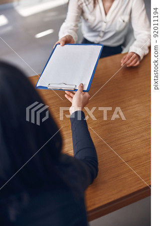 Smiling caucasian dark haired caucasian lady is filling a document on clinic's reception Smiling caucasian dark haired caucasian lady is filling a document on clinic's reception 92011194