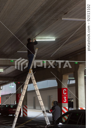 City Worker electrician repairs LCD lamp on mall parking. 92013102
