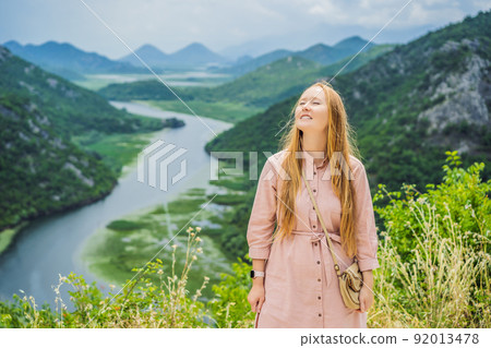 Woman tourist in the background Canyon of Rijeka Crnojevica river near the Skadar lake coast. One of the most famous views of Montenegro. River makes a turn between the mountains and flows backward 92013478
