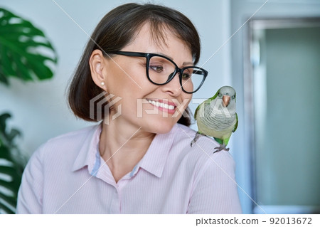 Middle aged woman at home with a pet parrot on her shoulder 92013672