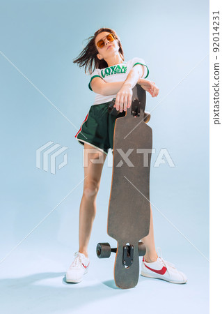 Portrait of stylish young woman in casual summer outfit posing with skateboard isolated over light blue background 92014231