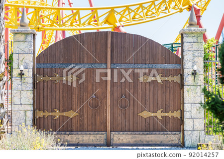 Wooden fabulous rounded gates in medieval style in an amusement park on a sunny day. Wooden fabulous rounded gates in medieval style in an amusement park on a sunny day. 92014257