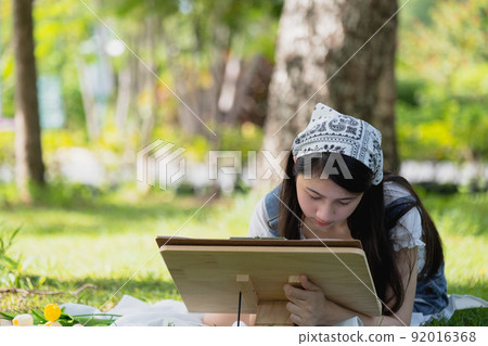 Young asian woman pianting and relaxing in park. 92016368
