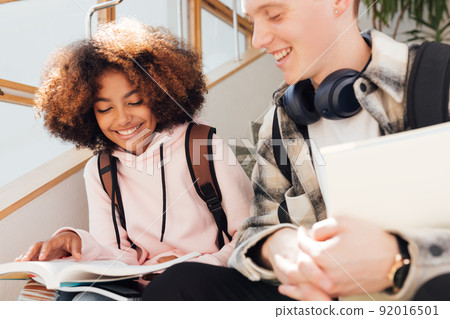 Cropped shot of two classmates sitting on stairs preparing assignments and smiling 92016501