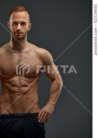 Croped shot of Young male athlete posing. Handsome athletic male power guy. Fitness muscular person. Young athlete showing muscles in the studio, posing shirtless on gray background. 92016688
