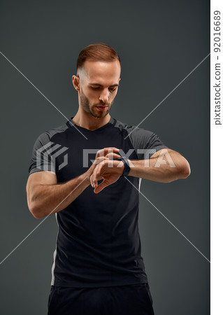 Sportsman checking heart rate on fitness tracker when training studio shot on gray background 92016689