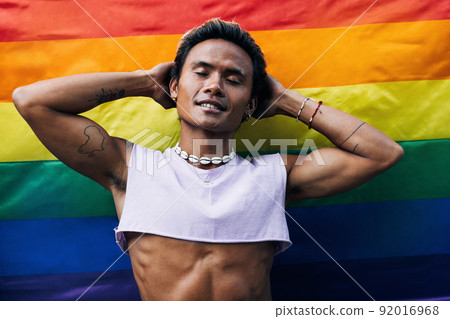 Guy posing on LGBT flag. Laughing male standing against rainbow flag.	 92016968