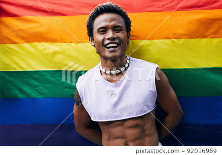 Guy posing on LGBT flag. Laughing male standing against rainbow flag. Guy posing on LGBT flag. Laughing male standing against rainbow flag. 92016969