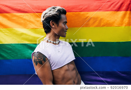 Guy posing on LGBT flag. Laughing male standing against rainbow flag.	 92016970