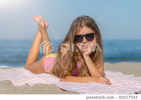 A teenage girl in a swimsuit and glasses lies on the beach. A teenage girl in a swimsuit and glasses lies on the beach. 92017593