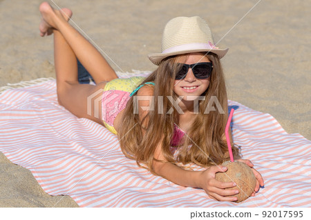 A teenage girl with a coconut lies on a beach towel on the seashore. A teenage girl with a coconut lies on a beach towel on the seashore. 92017595
