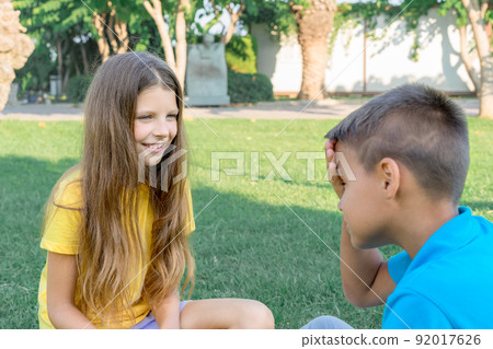Two teenage friends, a boy and a girl, communicate in a summer green park on a sunny day. 92017626