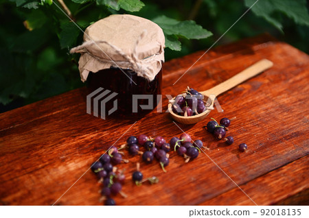 Still life of a jar of a homemade confiture, wooden spoon and gooseberries on a rustic wood surface. Culinary traditions 92018135