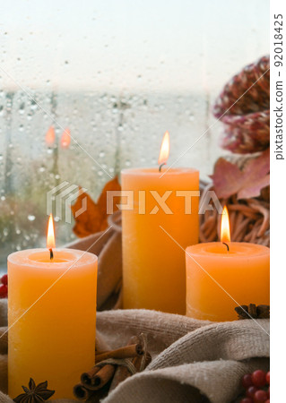 Hello Fall, celebrating autumn holidays at cozy home on the windowsill Hygge atmosphere Thanksgiving leaves, spices and candle on cozy knitted sweater in warm yellow lights. Raining Outside the window Hello Fall, celebrating autumn holidays at cozy home on the windowsill Hygge atmosphere Thanksgiving leaves, spices and candle on cozy knitted sweater in warm yellow lights. Raining Outside the window 92018425