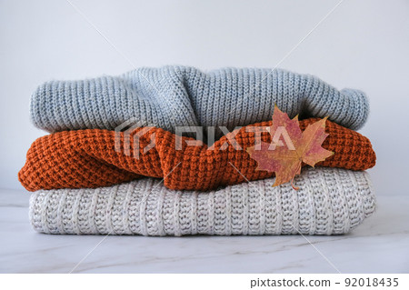 Stack of cozy knitted warm sweater with Autumn fall maple leaf. Sweaters in retro Style. Orange and blue colors. Cozy hygge concept Copy space 92018435