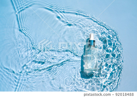Moisturizing cosmetic serum in transparent bottle with a dropper in water waves, blue background 92018488