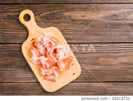 Pieces of smoked pork bacon meat food on a cutting board on wooden background, mockup. Copy space 92018732