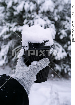 Female hand in winter warm gloves holding black eco paper cup. Winter picnic outdoors. Creative trendy zero waste recycle cup. Mockup. Hot warming drink to go in winter day. Take away concept 92018751