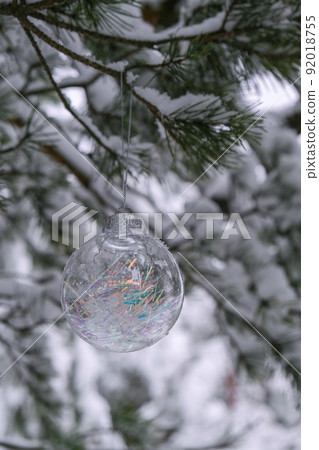 Transparent trendy glass Christmas ball on snowy branch firs in winter forest. Winter holiday background. Copy space. Happy new year Merry Christmas greeting card. Snow falling in background 92018755