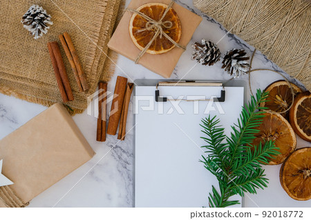 Woman preparing for christmas holidays. Writing gift list. Box with New Year's gifts, wrapped in craft paper and decorated with fir branch, dry orange slices, cinnamon sticks. Handmade Eco friendly Woman preparing for christmas holidays. Writing gift list. Box with New Year's gifts, wrapped in craft paper and decorated with fir branch, dry orange slices, cinnamon sticks. Handmade Eco friendly 92018772