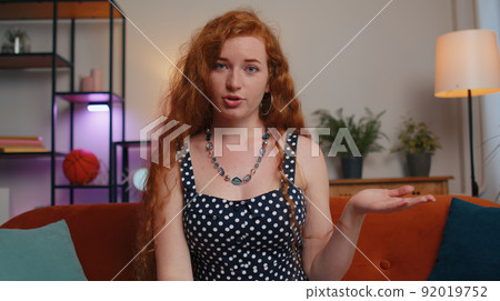 Woman sitting on home couch, looking at camera, making video conference call with friends or family Woman sitting on home couch, looking at camera, making video conference call with friends or family 92019752