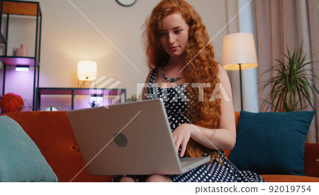 Redhead girl freelancer starts working on laptop, sends messages, makes online purchases at home Redhead girl freelancer starts working on laptop, sends messages, makes online purchases at home 92019754