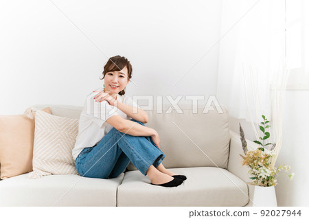 (Looking at the camera) A Japanese woman in jeans sitting on the sofa at home and relaxing 92027944
