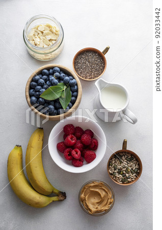 Banana and berry smoothie ingredients made from fresh banana, blueberry, raspberry, milk, peanut butter, chia seeds, almond flakes. Top view 92033442
