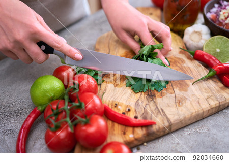 making salsa dip sauce - woman cutting and chopping cilantro or parsley on wooden cutting board 92034660