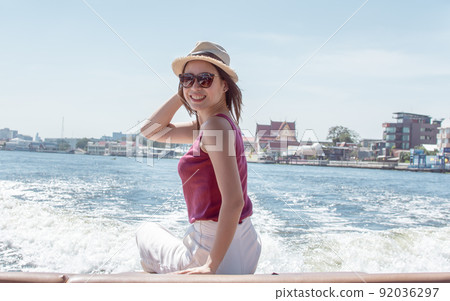 Asian woman waving her hand while sitting on boat Asian woman waving her hand while sitting on boat 92036297