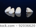 four dental crowns zirconia on a mirror table, black background. crowns for front teeth. 92036620