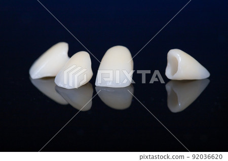 four dental crowns zirconia on a mirror table, black background. crowns for front teeth. four dental crowns zirconia on a mirror table, black background. crowns for front teeth. 92036620